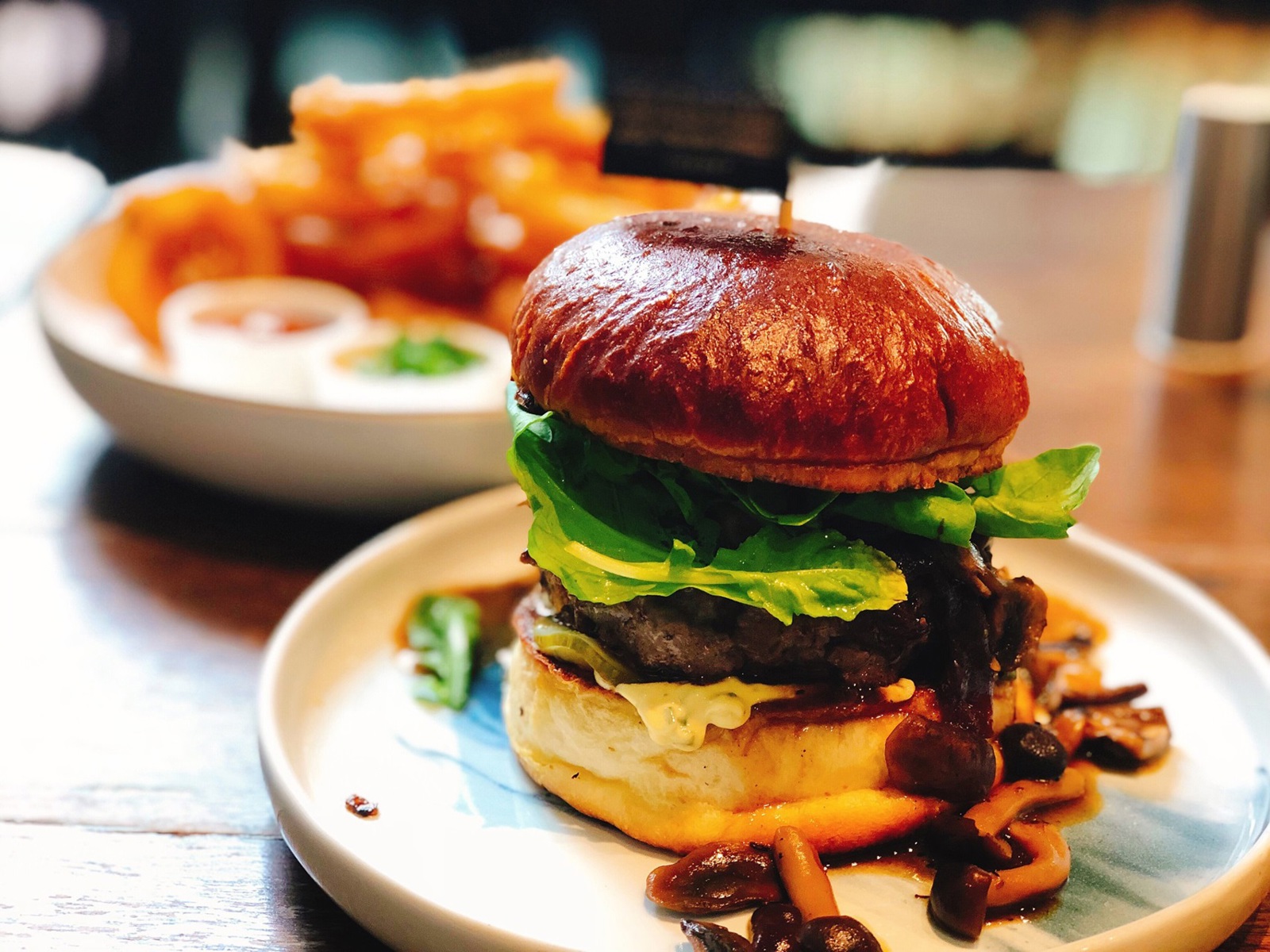 mushroom and beef burger with fried onion rings in the background